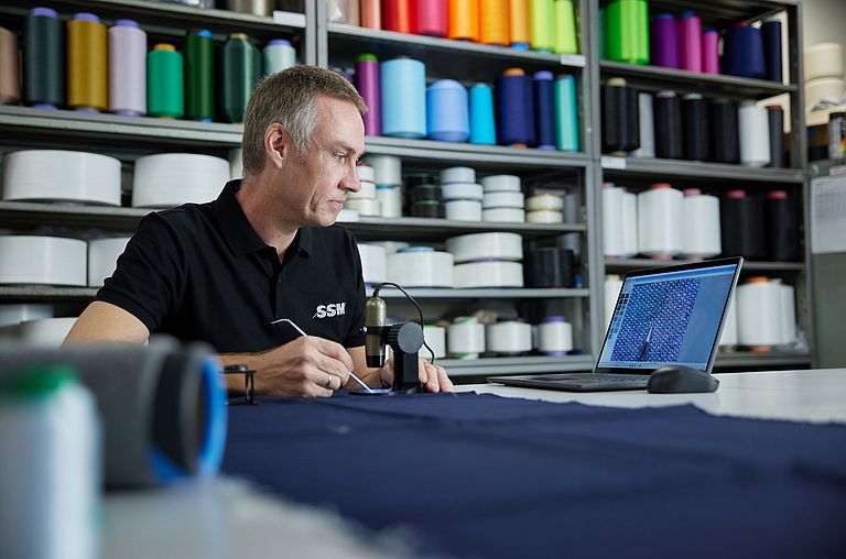 SSM textile technologist examining yarn samples under a microscope to provide expert recommendations to customers.